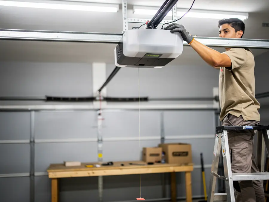 A technician on a ladder installs a garage door opener in a garage.